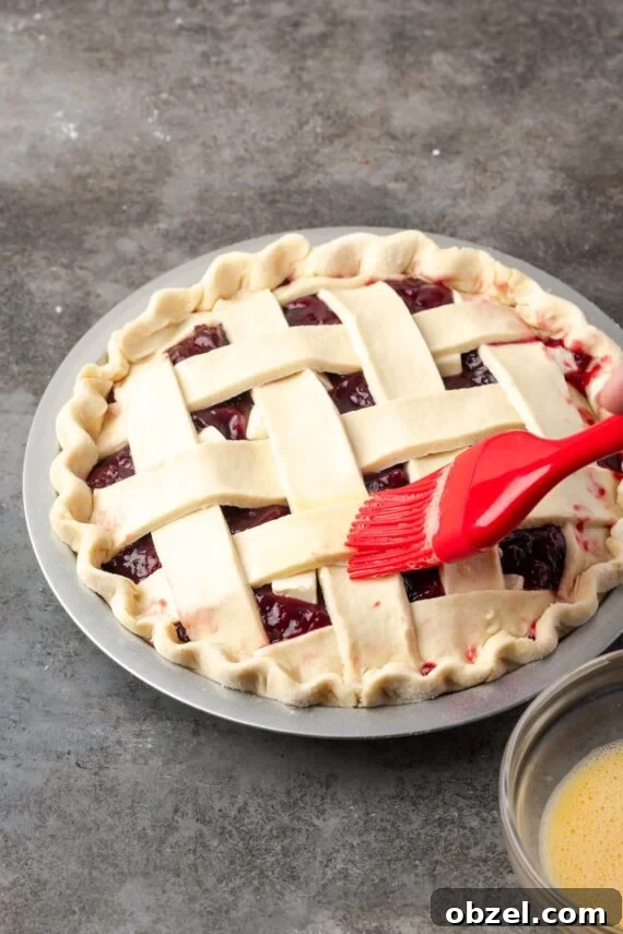 Brushing egg wash over cherry pie crust. A red rubber spatula is used to brush egg wash over a lattice pie crust.