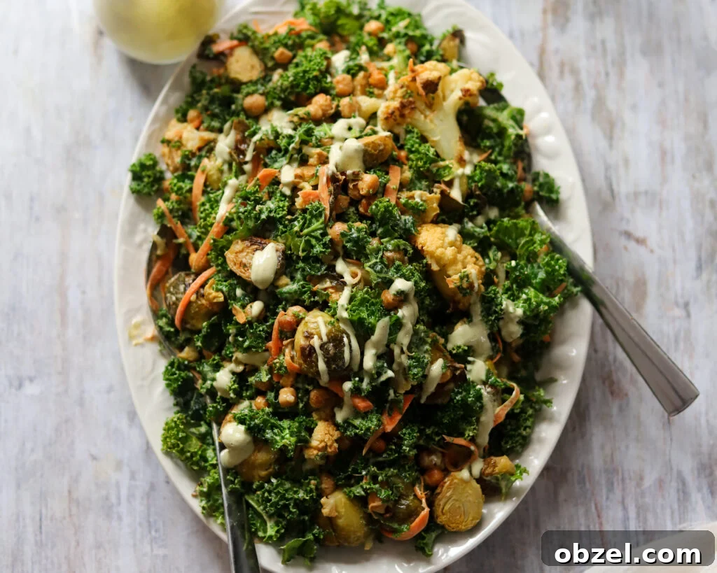 Overhead view of a huge platter of kale salad with roasted cauliflower and brussels sprouts, chickpeas and creamy tahini dressing