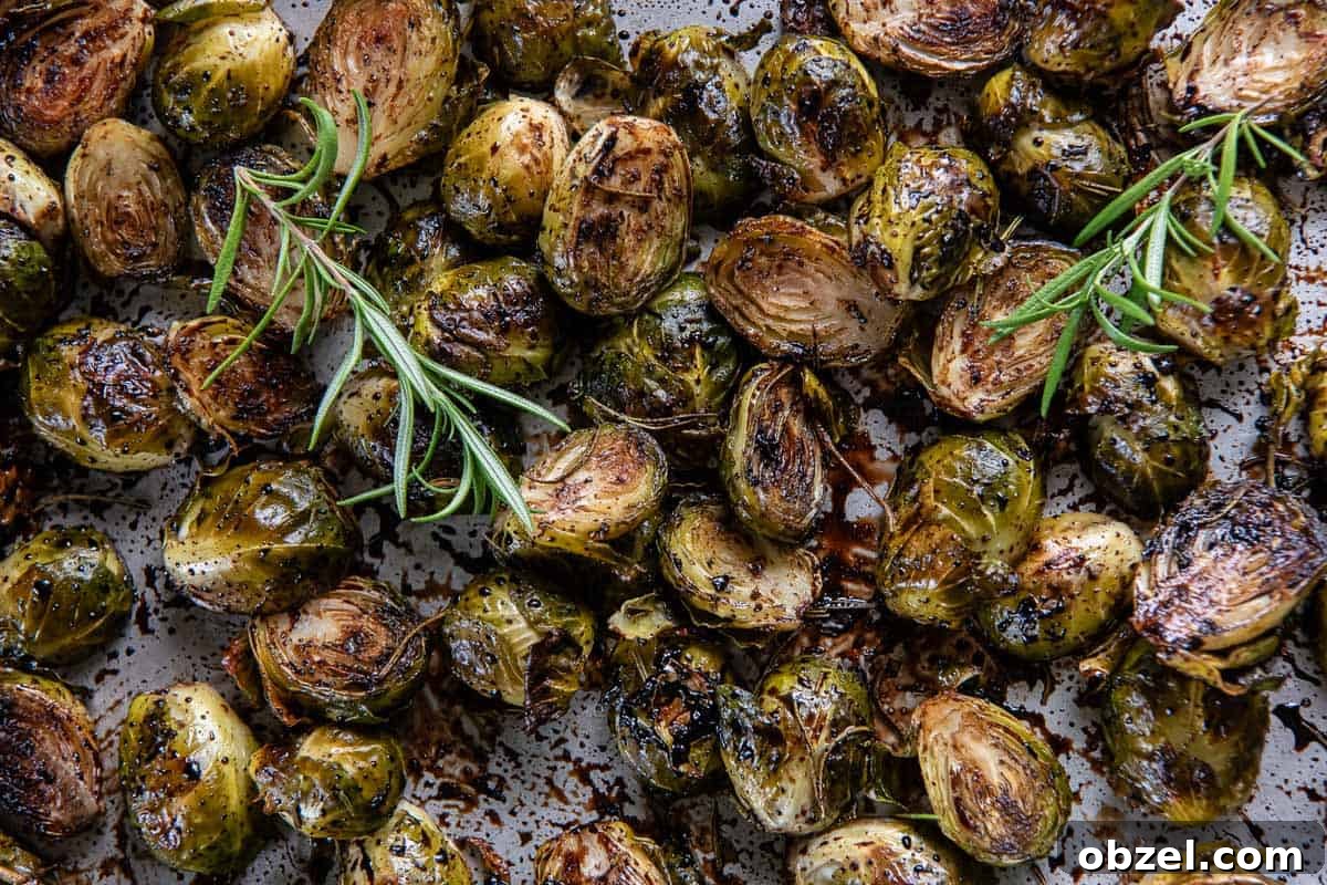 Roasted brussels sprouts with sprigs of rosemary and balsamic glaze on a baking sheet.