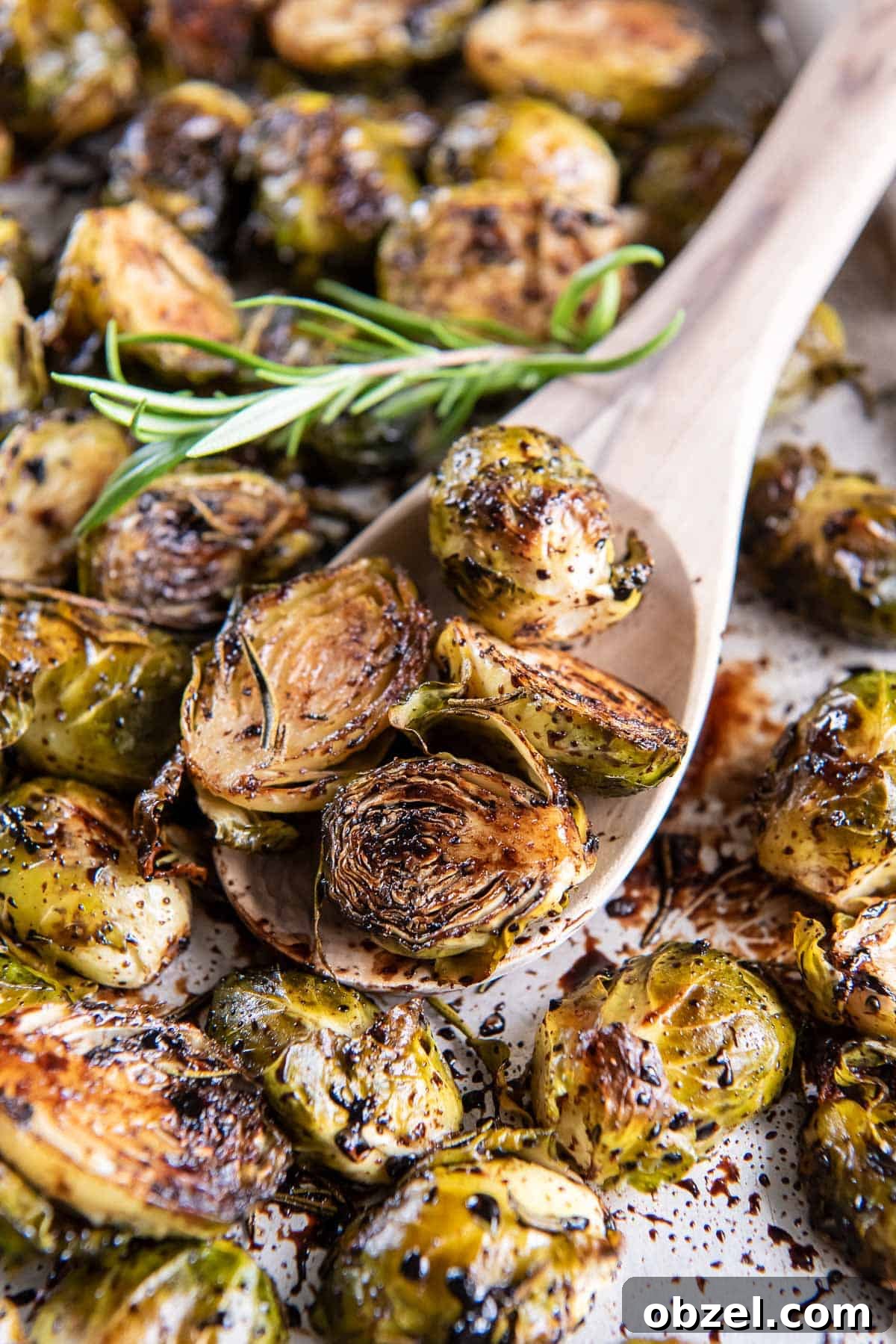 A wooden spoon scooping roasted brussels sprouts from a baking sheet.