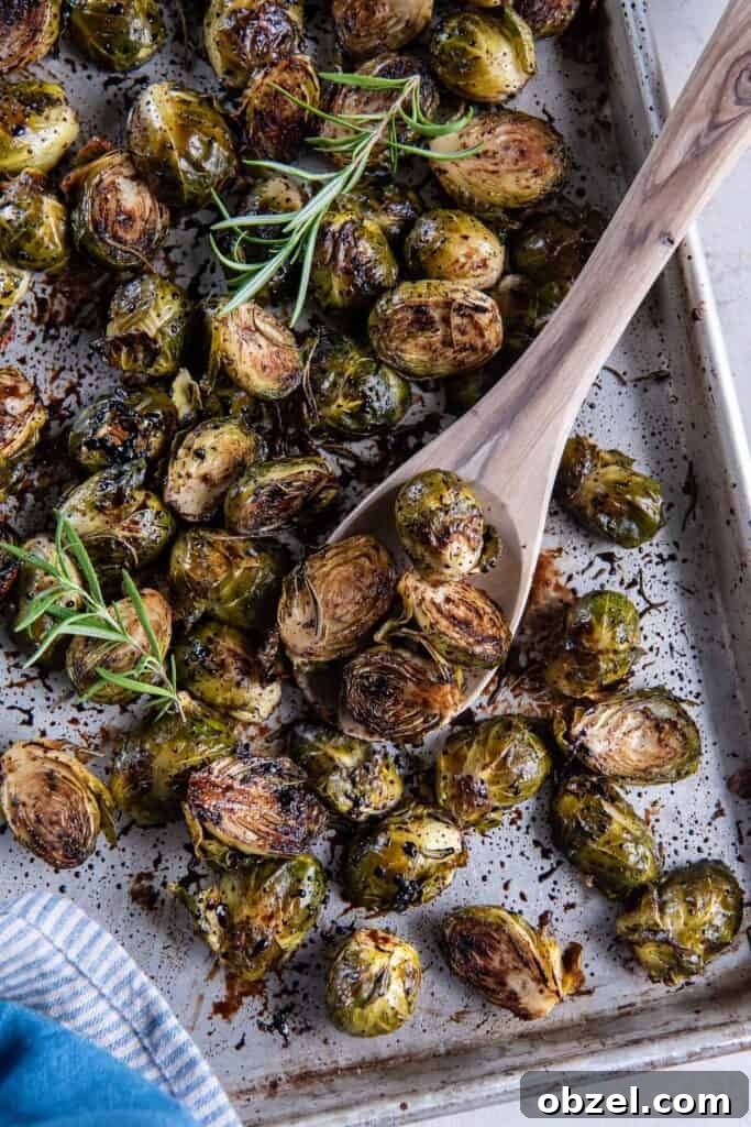 A wooden spoon scooping roasted brussels sprouts from a baking sheet.