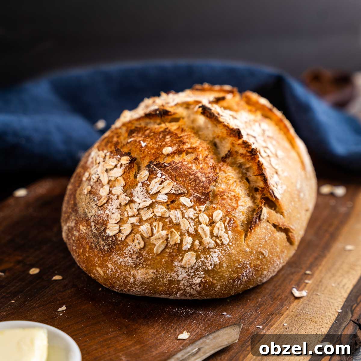 A golden brown loaf of rye sourdough bread topped with oats on a cutting board - hostess at heart