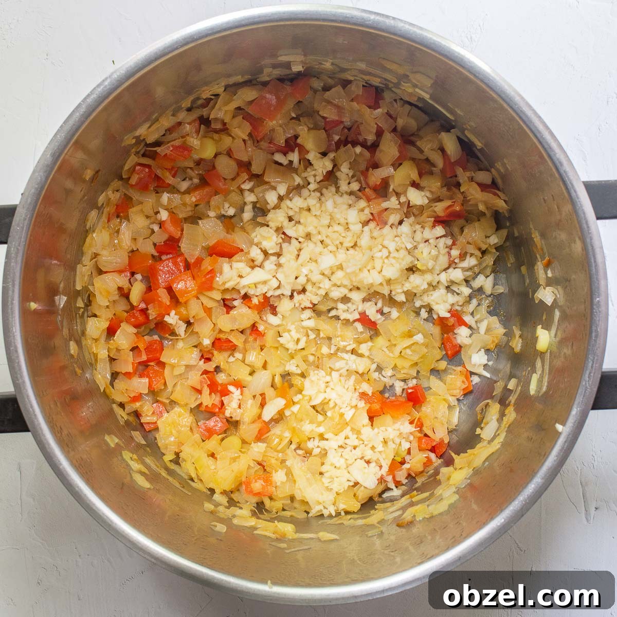 Traditional Spanish Lentil Stew with Chorizo 7 Fried red pepper and onions in a large steel pot, with raw chopped garlic on top.