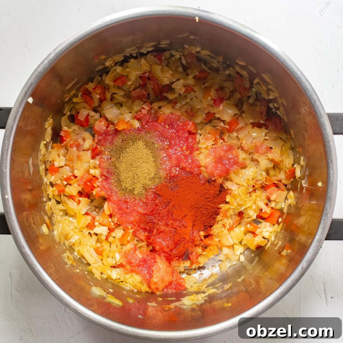 Traditional Spanish Lentil Stew with Chorizo 8 Fried onion and peppers in a large steel saucepan with added grated tomato and spices.
