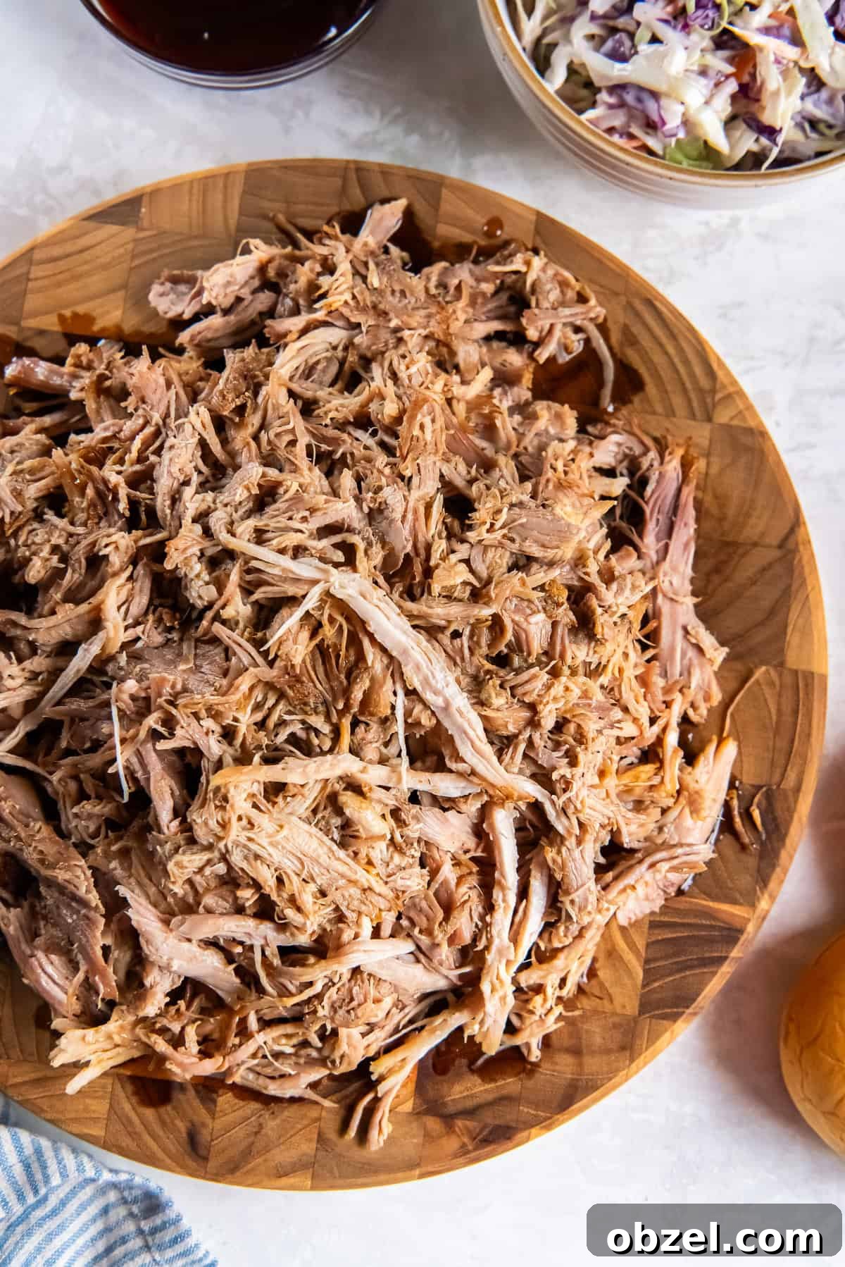 Slow Cooker Pulled Pork Recipe 2 Slow cooker pulled pork shredded and piled on a wooden board with barbecue sauce and coleslaw in the background.
