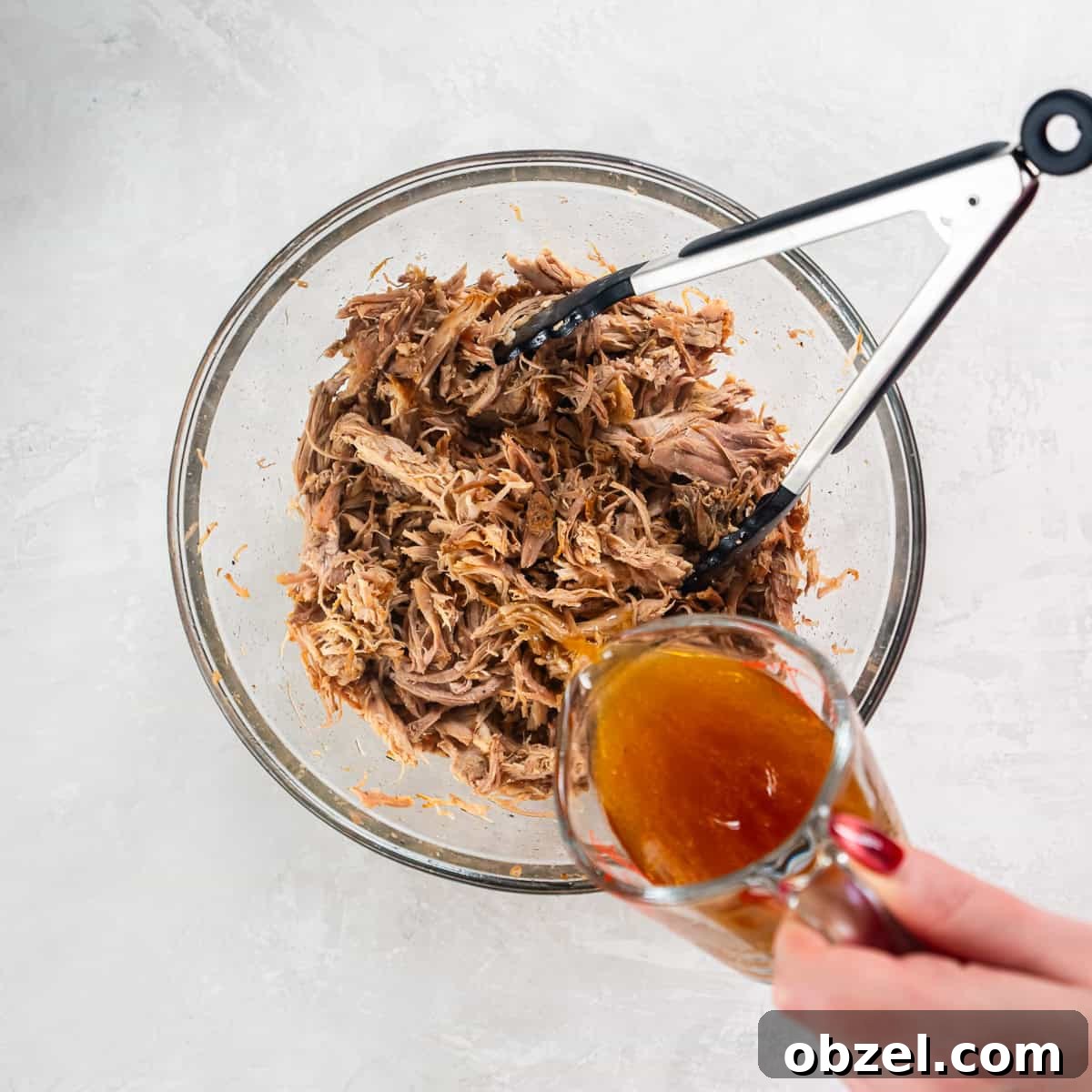 Slow Cooker Pulled Pork Recipe 12 Shredded pulled pork being moistened with juices in a bowl.