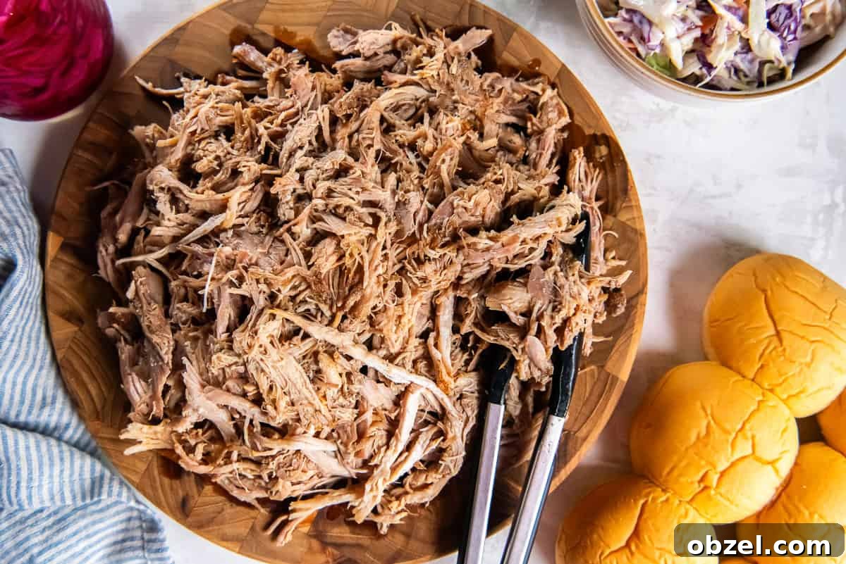 Slow Cooker Pulled Pork Recipe 13 Shredded slow cooker pulled pork on a wooden board with slider buns and coleslaw on the side.