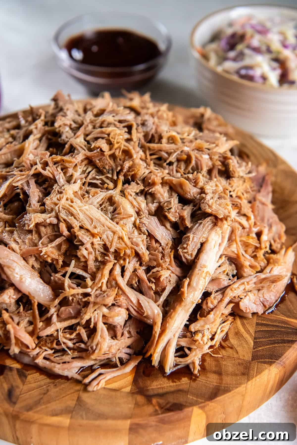 Slow Cooker Pulled Pork Recipe 14 Slow cooker pulled pork served on a wooden board with barbecue sauce and coleslaw in the background.