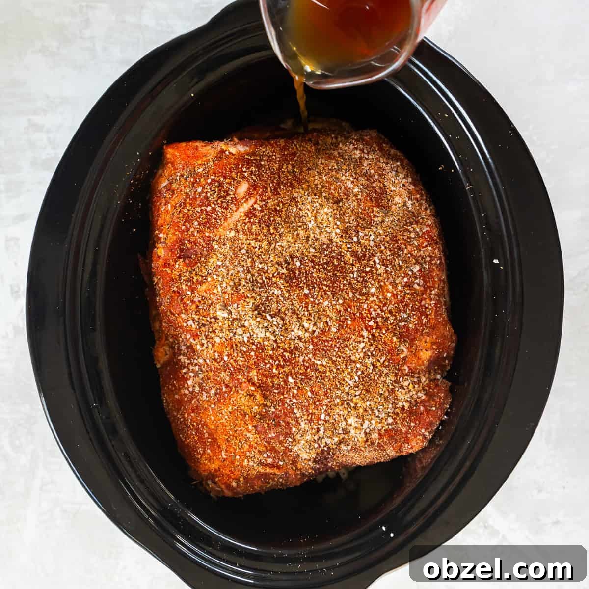 Slow Cooker Pulled Pork Recipe 7 Seasoned pork shoulder placed over onions in a slow cooker with cooking liquid being added.