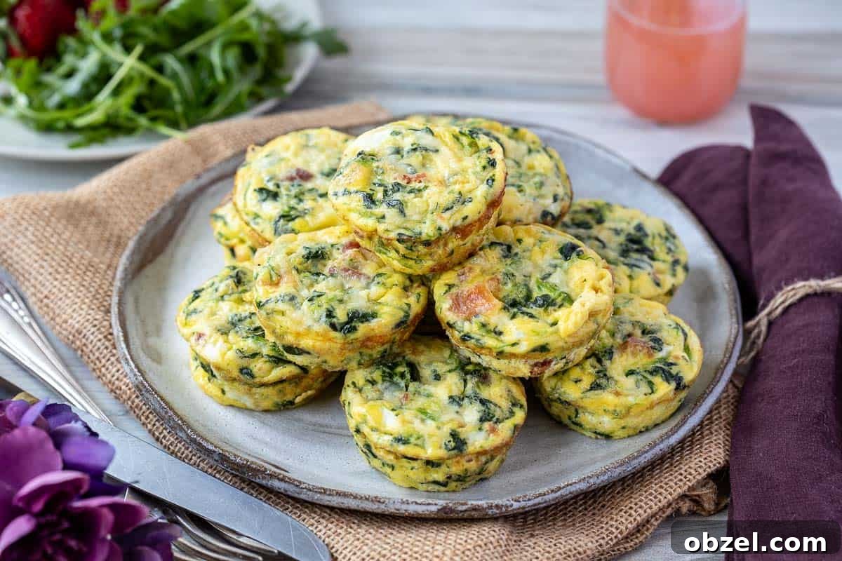 Mini Spinach Egg Bites: Oven-Baked Breakfast Recipe 7 A plate of spinach bacon egg cups stacked neatly. A salad and glass are in the background on a wooden table.