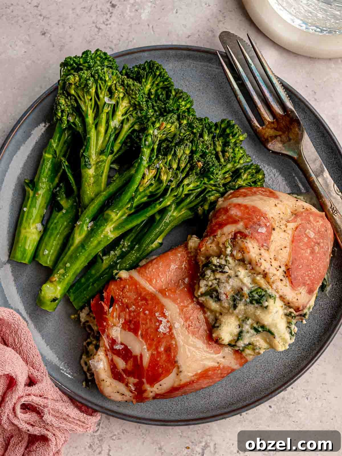 Chicken wrapped in prosciutto with broccolini on a blue plate.