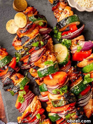 Grilled teriyaki chicken kabobs served on a slate board with sesame seeds.