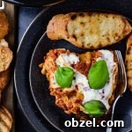 Slice of homemade lasagna with fresh mozzarella, basil, and garlic bread.