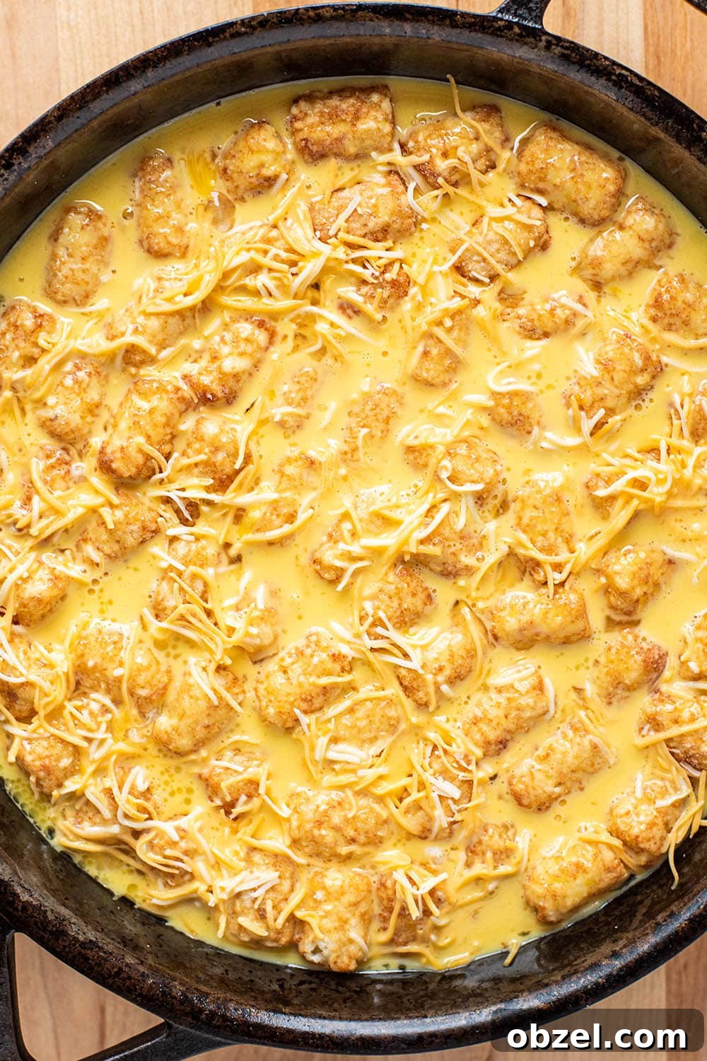 Tater Tot Breakfast Casserole with Eggs and Sausage 4 Whisked egg and shredded cheese poured over tater tots in a cast iron skillet.