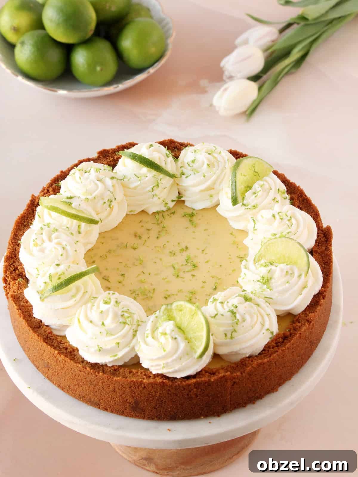 Key Lime Pie Recipe with Graham Cracker Crust 9 Key lime pie placed on cake stand with limes and white tulips in background.