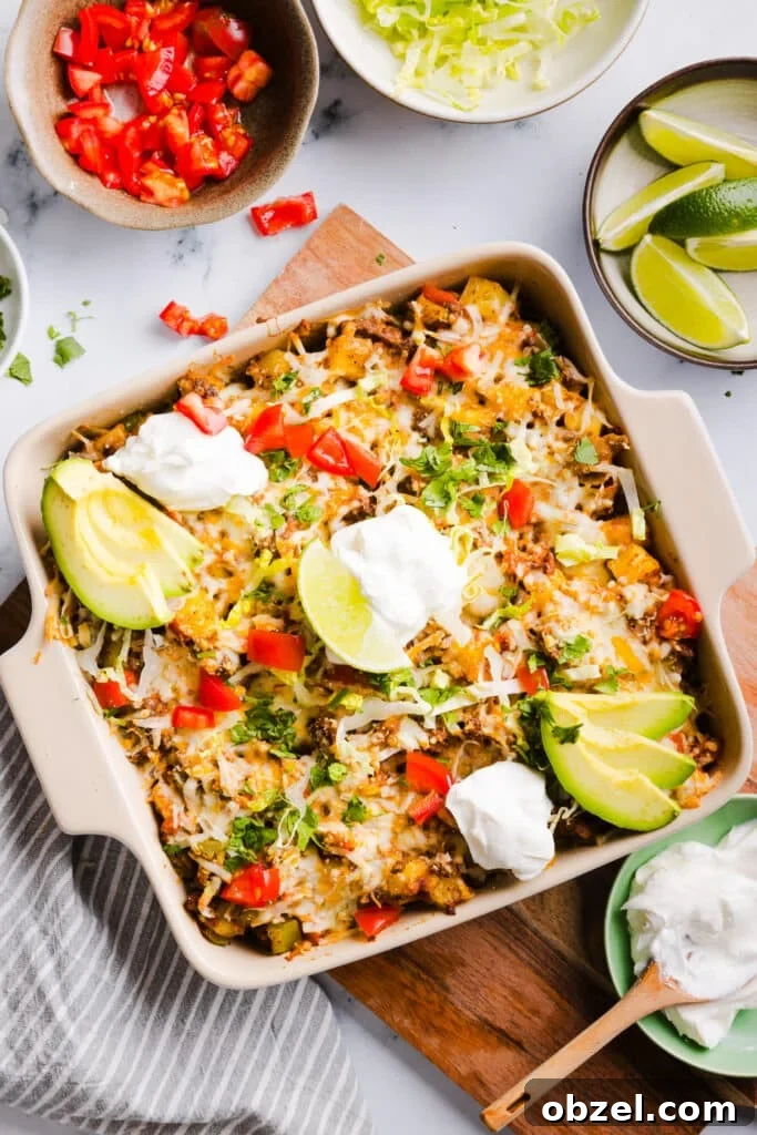 High-Protein Cheesy Taco Potato Casserole 2 Taco potato casserole baked in a dish and topped with shredded lettuce, cheese, sour cream, avocado, lime and tomatoes.