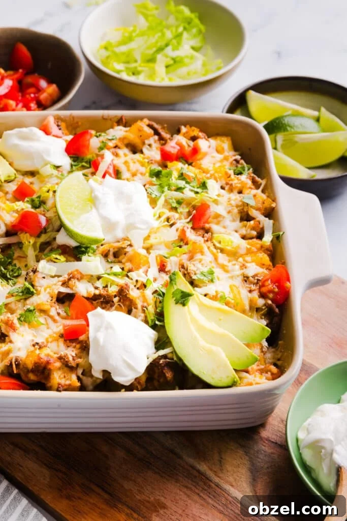 High-Protein Cheesy Taco Potato Casserole 9 Taco potato casserole baked in a dish and topped with shredded lettuce, cheese, sour cream, avocado, lime and tomatoes.