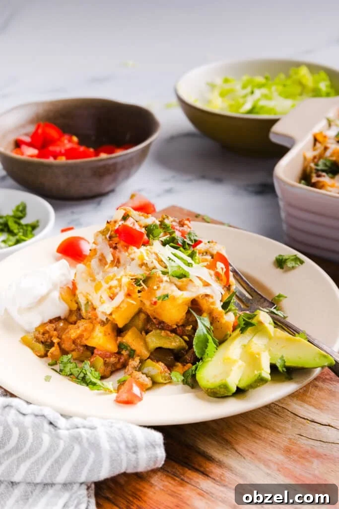High-Protein Cheesy Taco Potato Casserole 10 Taco potato casserole plated and topped with avocado, tomatoes and sour cream.