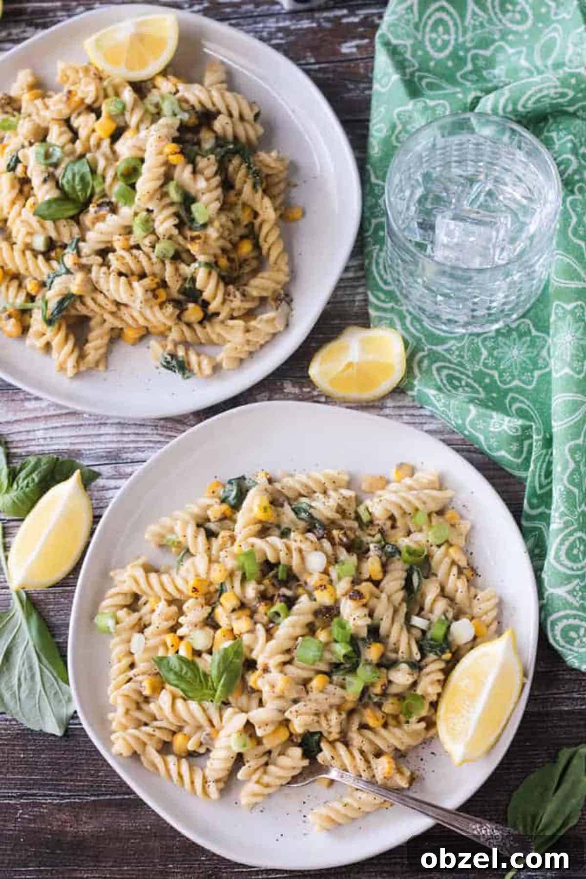 Two plates of rotini pasta with corn kernels and basil.