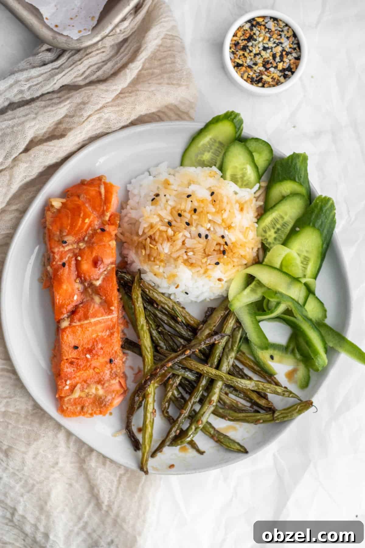 A plate with salmon, rice, cucumbers and green beans.
