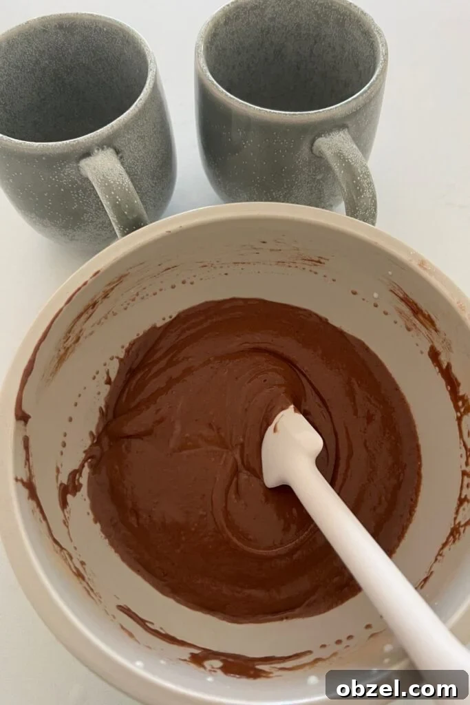Quick Sourdough Discard Mug Cake Recipe 4 Sourdough chocolate cake batter mixed in a bowl with two stoneware mugs behind it.