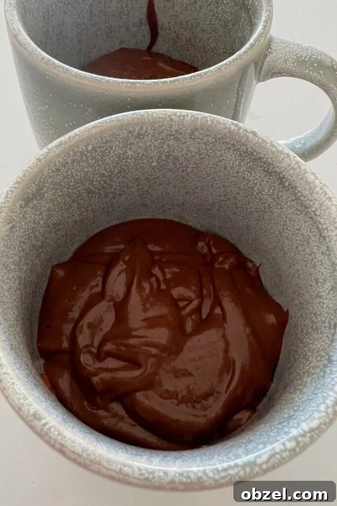 Quick Sourdough Discard Mug Cake Recipe 5 Glossy chocolate sourdough cake batter being added to mugs before microwaving.
