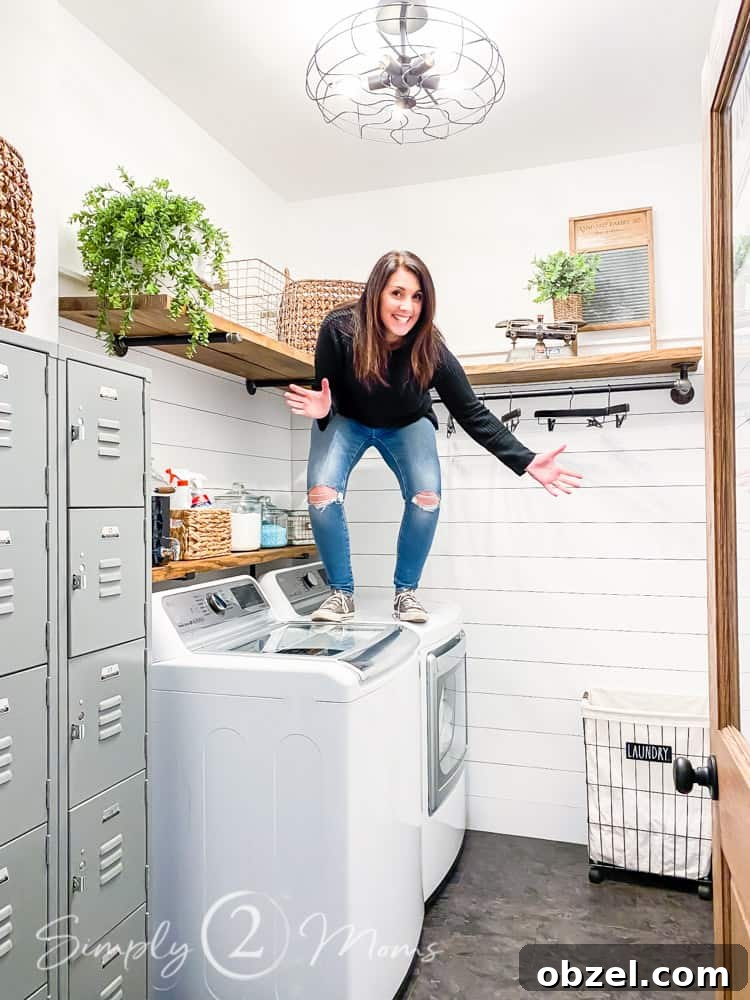 Stunning Before and After Laundry Room Makeover 15 woman standing on dryer in completed laundry room transformation. washer dryer vintage lockers on left side of room wood shelves over washer and dryer and along back wall shiplap on walls