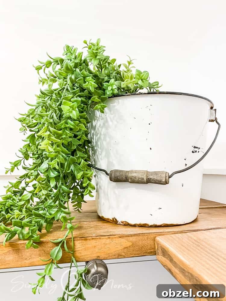 Stunning Before and After Laundry Room Makeover 17 close up of vintage metal bucket with wood handle and faux greenery in bucket spilling out and onto diy shelves