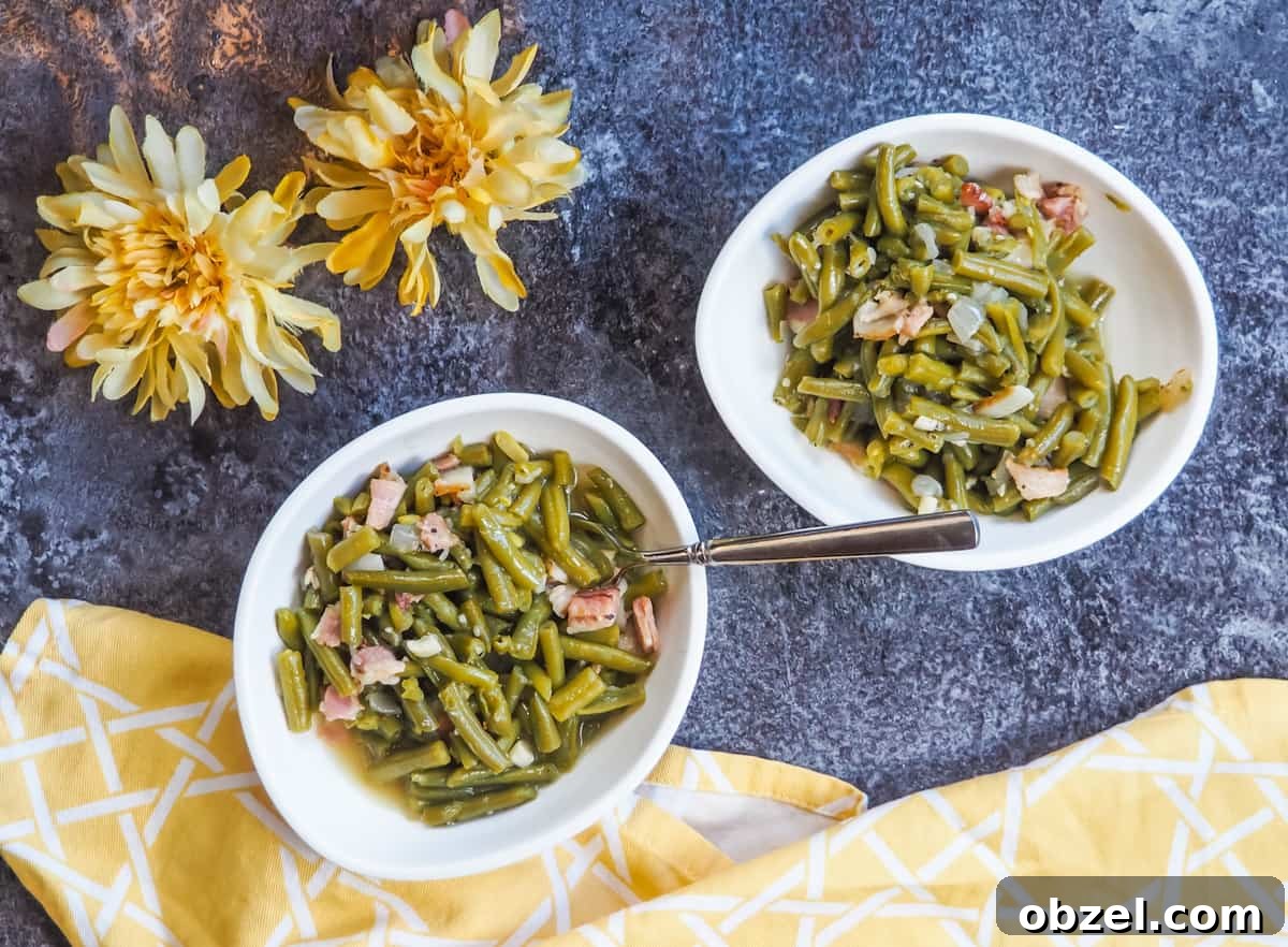 Two white bowls with southern green beans and bacon on a gray background with two yellow flowers and a yellow napkin.