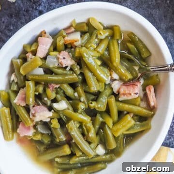 A white bowl of southern green beans and bacon on a gray background.