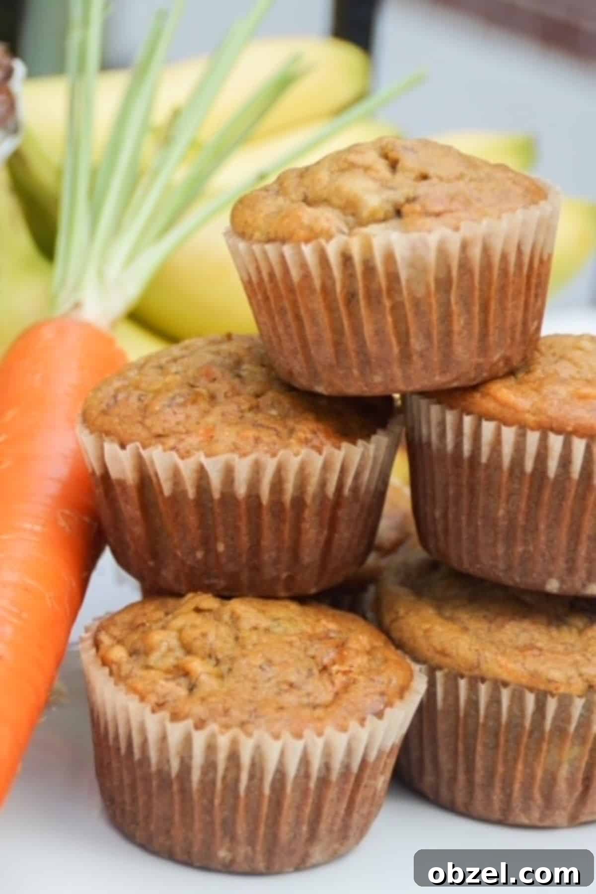 Stacked muffins with a carrot and bananas in the background