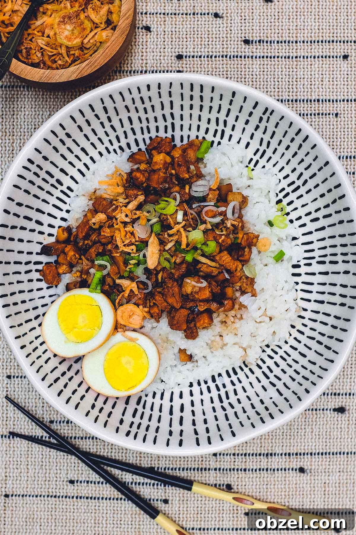 A bowl of Taiwanese braised pork (Lu Rou Fan) on a bed of rice with two egg halves, crispy onion and spring onions as a garnish.