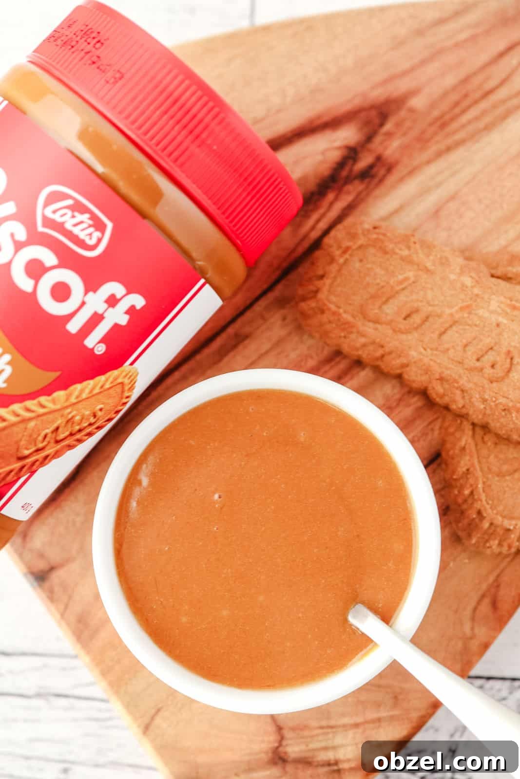 Biscoff Cookie Butter Sauce Recipe 5 Top down view of Biscoff topping in a serving bowl with a spoon in it, with Biscoff cookies and a jar of Biscoff spread on the side.