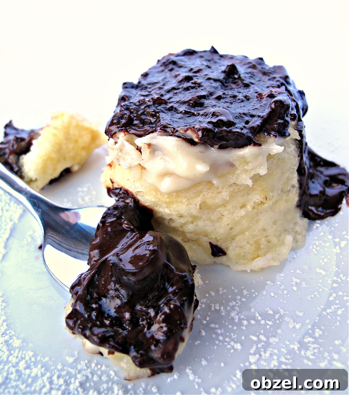 Boston Cream Pie Mug Cake on a plate behind a spoon full of cake covered in melted chocolate.