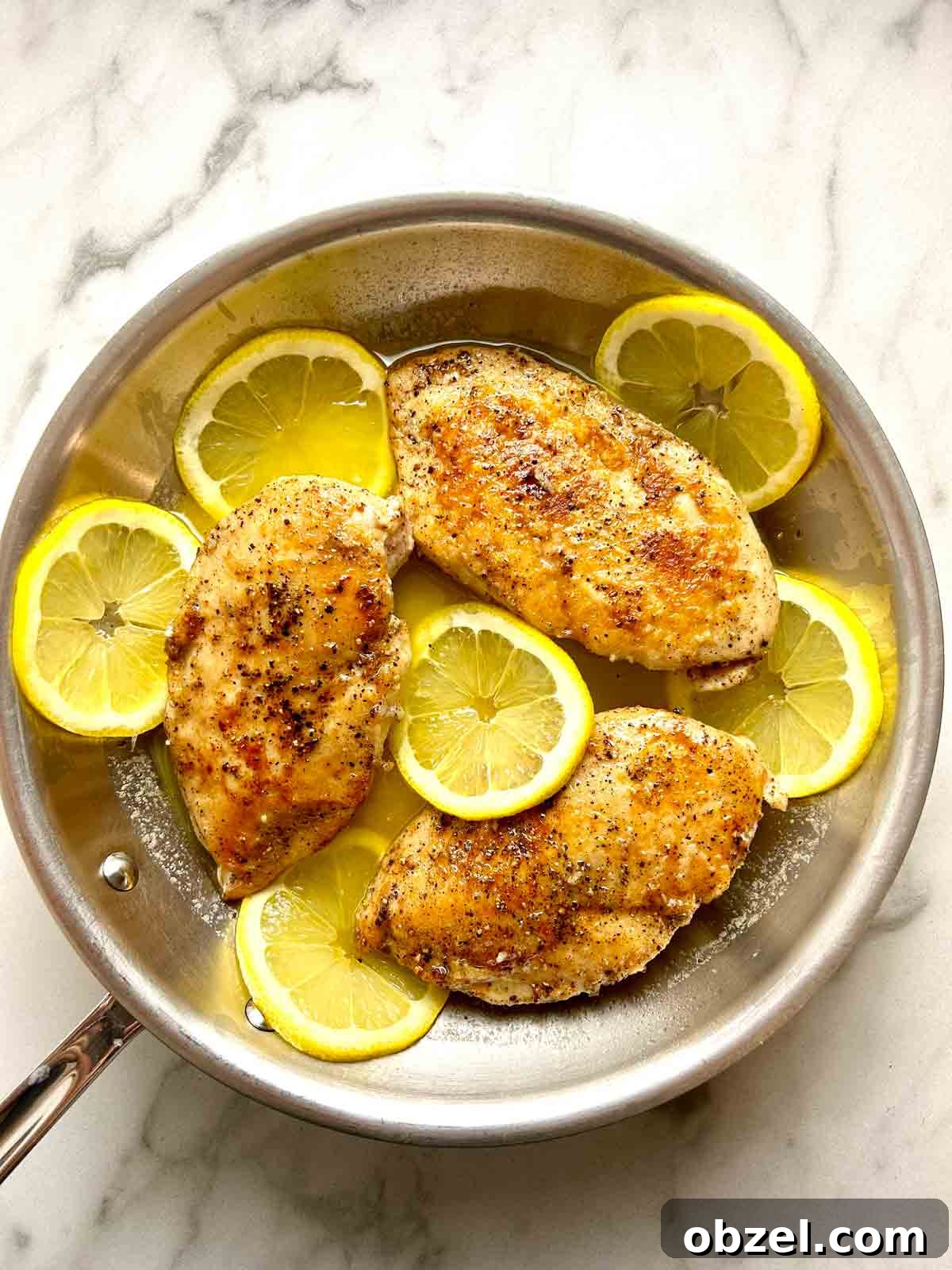 Juicy Lemon Pepper Chicken Breasts Recipe 2 lemon pepper chicken cooking in skillet with slices of lemon all over.