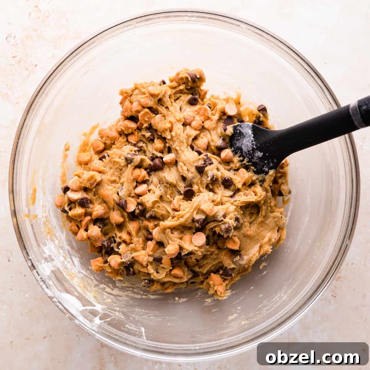 Butterscotch Chocolate Chip Cookie Recipe 6 glass mixing bowl with cookie batter with butterscotch and chocolate chips inside and a rubber spatula inside of the bowl.