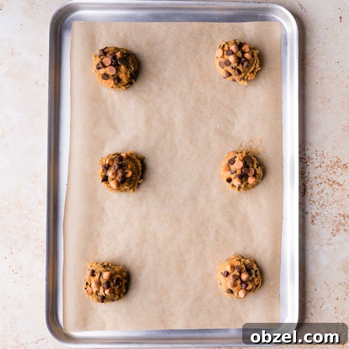 Butterscotch Chocolate Chip Cookie Recipe 7 large metal baking sheet lined with brown paper and 6 portions of butterscotch cookies dough on it.