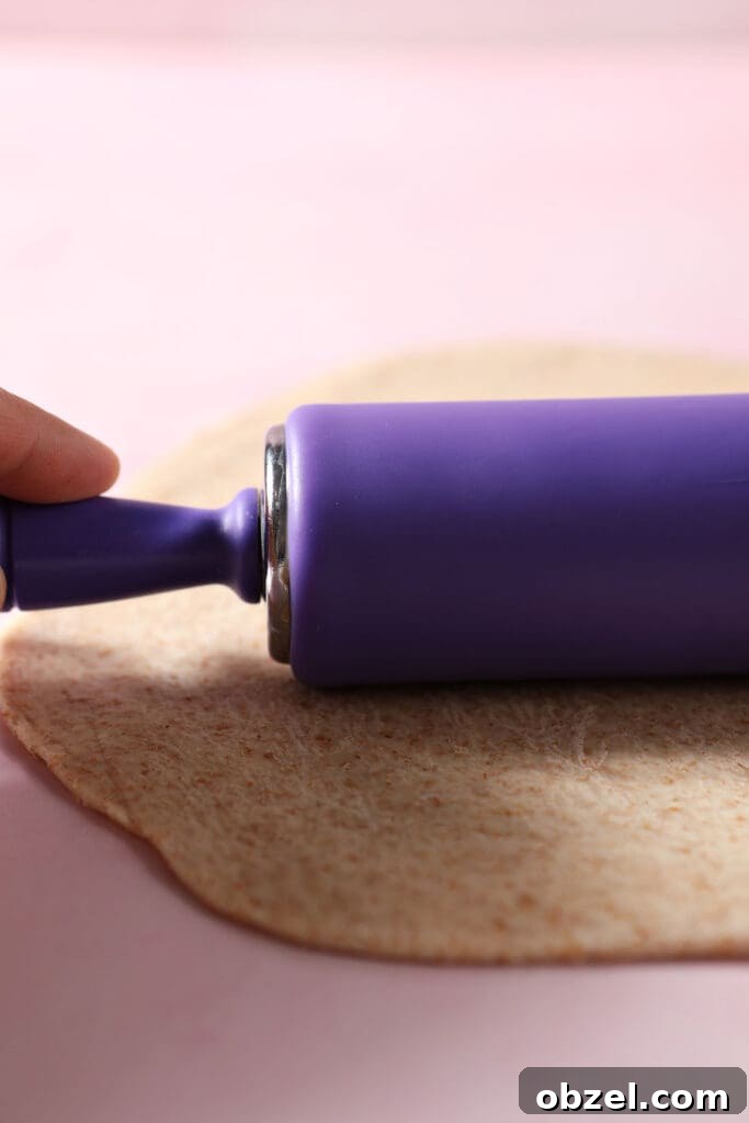 A purple rolling pin rolls out pizza dough on a pink surface