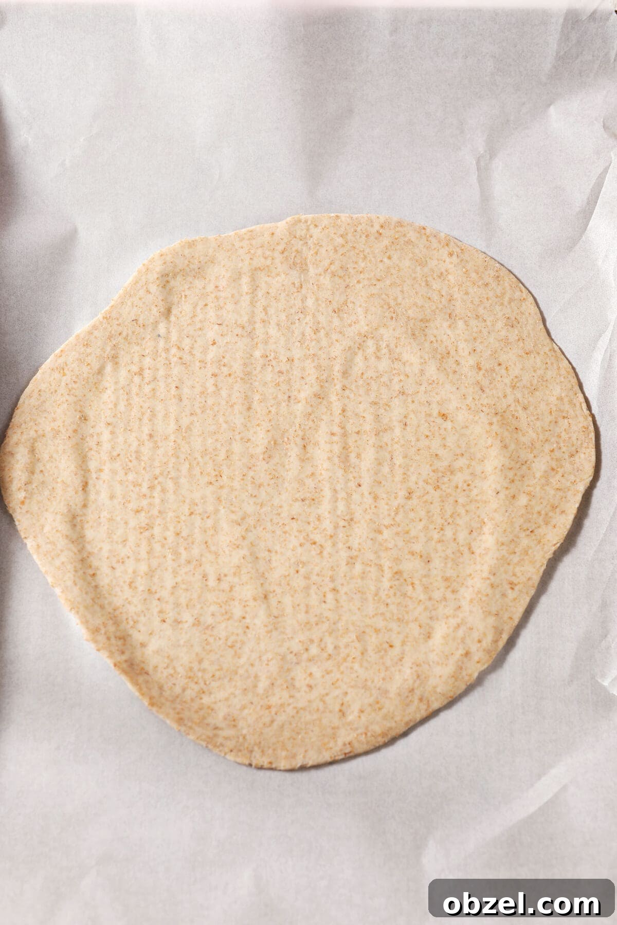 A rolled out round of pizza dough on parchment