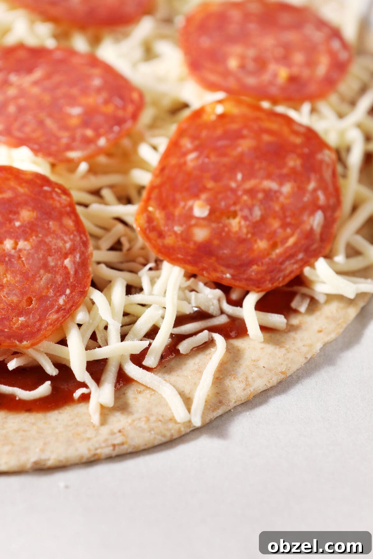 Close up of pizza dough topped with sauce, cheese and pepperoni on parchment before baking
