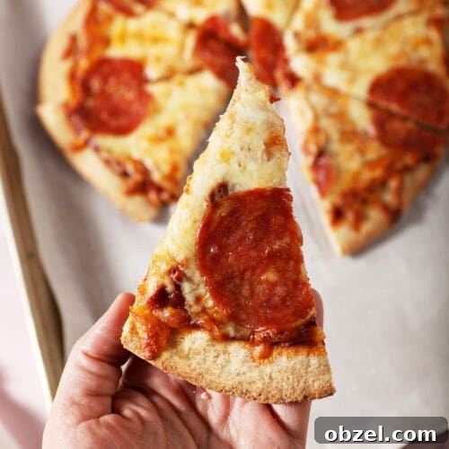 A hand holds a slice of homemade pepperoni pizza