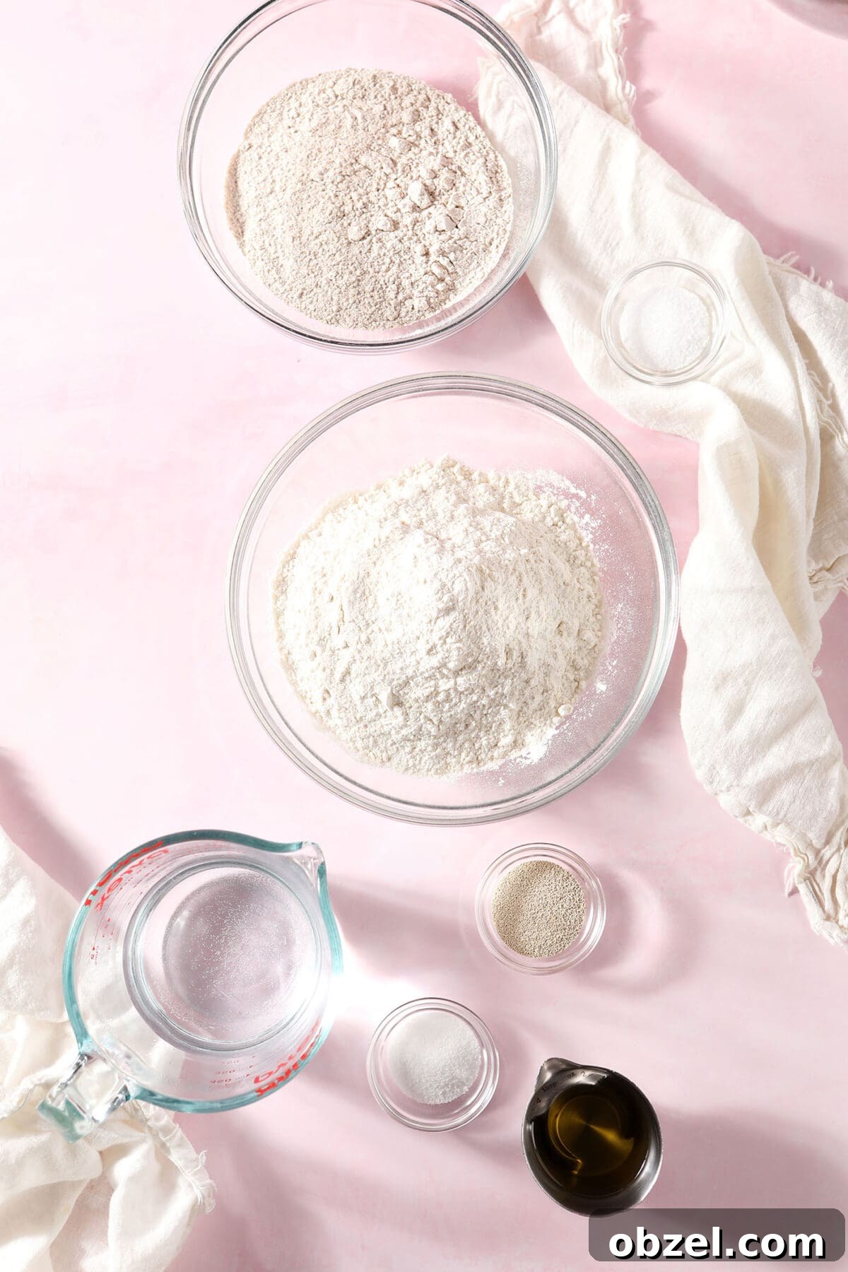 Ingredients to make homemade pizza dough in bowls on a pink surface