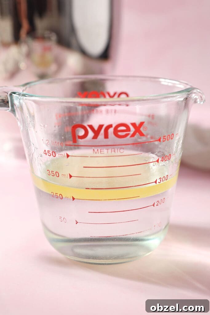 A liquid measuring cup of water, oil and sugar on a pink surface