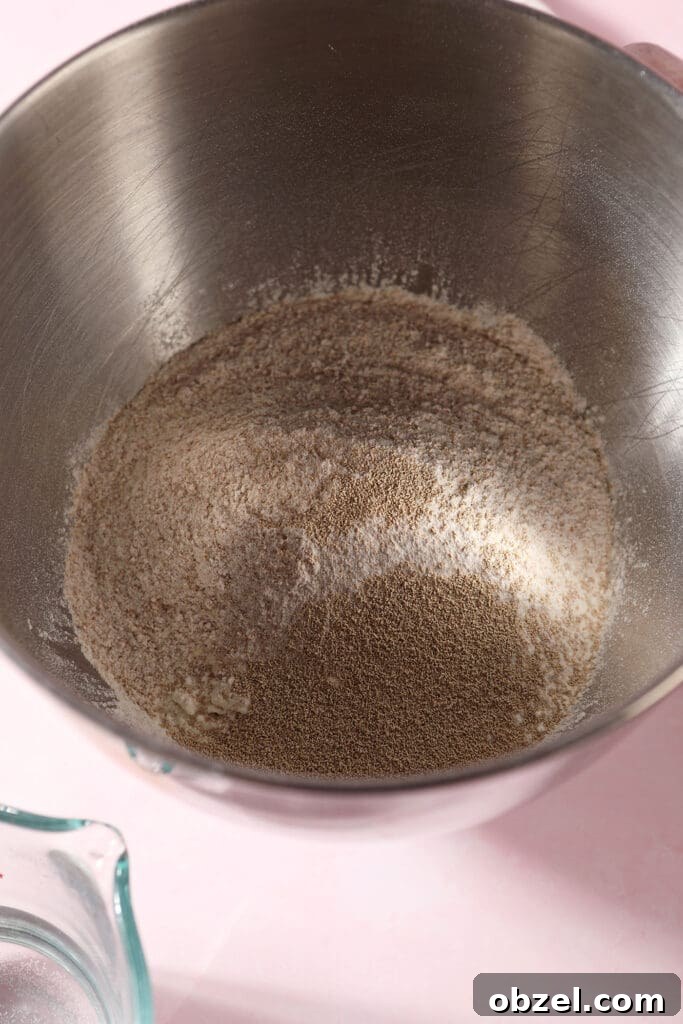 Flours and yeast in the bowl of a stand mixer on a pink surface