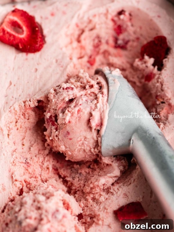 Container of strawberry ice cream with a scoop taken out using a stainless steel ice cream scoop.