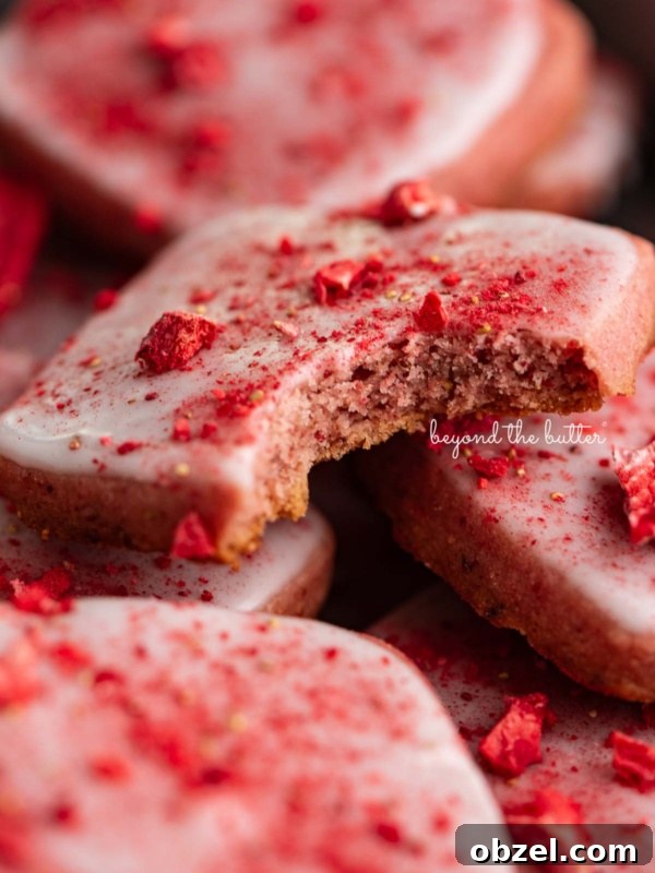 Strawberry shortbread cookies topped with glaze and freeze-dried strawberry bits randomly placed in a vintage baking tin.