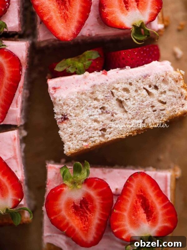 Slices of mini strawberry sheet cake topped with strawberry buttercream frosting and fresh strawberries with one slice on its side.