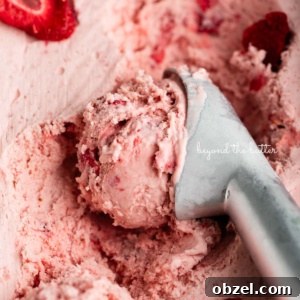 Container of strawberry ice cream with a scoop taken out using a stainless steel ice cream scoop.