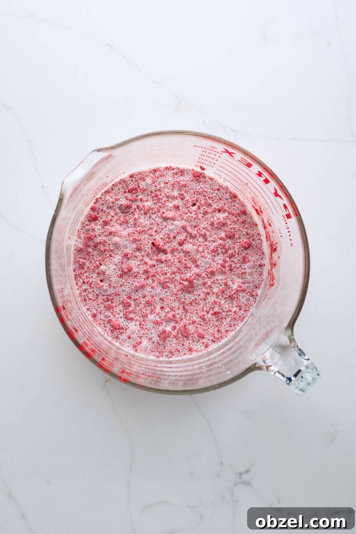 Strawberry ice cream base mixed all together in a large glass mixing bowl on a white marbled background.