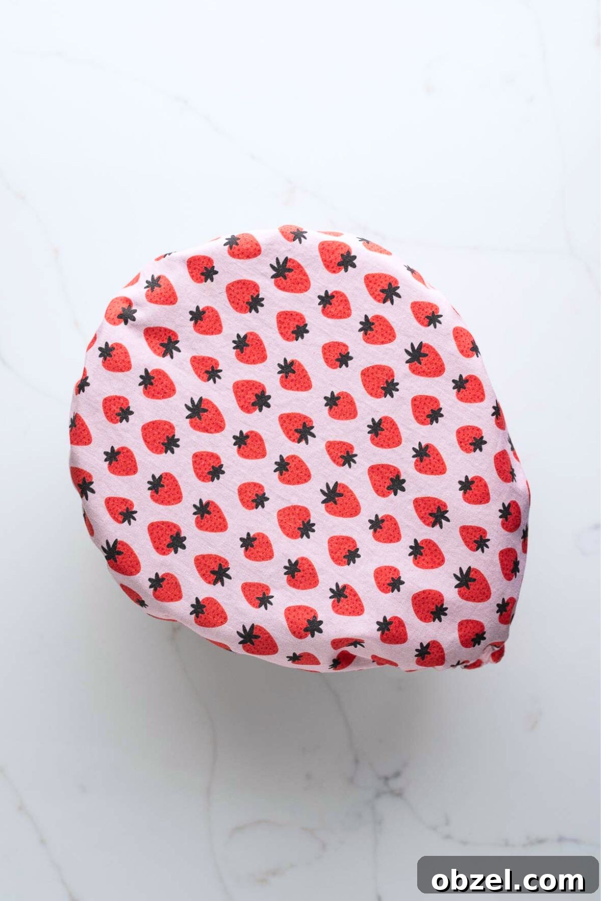 Strawberry print cover placed over large glass mixing bowl on white marbled background.
